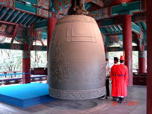 이미지는 약 3미터 높이의 종과 그 옆에 있는 축하객을 보여줍니다.