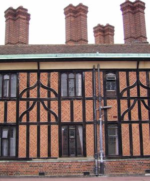 검은 목재와 붉은 벽돌로 만들어진 건물의 근접 사진입니다. 건물에는 4개의 키가 큰 벽돌 굴뚝이 있습니다. 비교적 현대적인 배수관이 건물 중앙으로 내려옵니다.