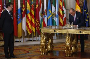 후안 카를로스 1세가 퇴위 법안에 서명하고 있다. 그 옆에는 법안에 공동 서명한 마리아노 라호이 총리가 있다. (2014년 6월 18일).