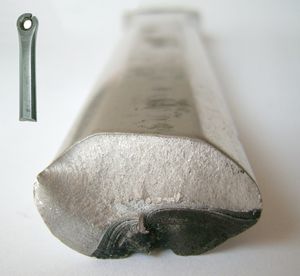 대략 달걀 모양의 금속 원통의 끝면을 정면에서 본 모습입니다. 금속 끝면의 오른쪽 하단 부분은 어둡고 약간 변형되어 있으며, 나머지는 훨씬 밝은 색상이고 변형되지 않았습니다.