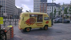 도시 광장에 와플 그림으로 장식된 노란색 밴이 있고 옆에는 판매 창문이 있다