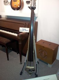 A museum exhibit of vintage musical instruments shows a 1930s amplifier and speaker cabinet and an upright bass with a pickup.