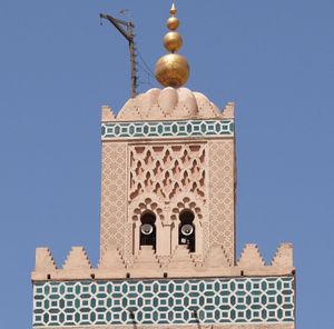 상부 미나레트의 디테일: 젤리 타일 작업의 프리즈가 주요 탑 축의 상단(하단)을 따라 이어지고, 더 작은 두 번째 축(상단)에는 세브카 패널과 모서리 주변에 밝은 색상의 기하학적 패턴이 있다. 구리 구체의 꼭대기가 정점을 이룬다.