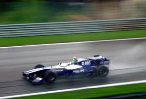 A dark blue and white Formula One being driven at high speed on a racing circuit