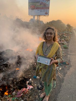 야외 불법 소각장 근처에서 공기질 측정을 하는 여성(인도 뭄바이)