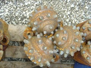 회전식 드릴 비트의 삼중 원뿔형 조립품. 롤러에 삽입된 돌출된 탄화 텅스텐 버튼을 보여준다.