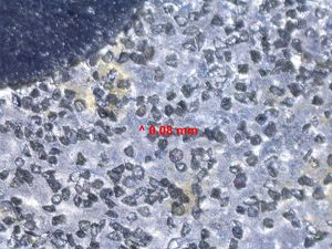 220 입자 다이아몬드 연마석의 취미 현미경 시야. 작은 다이아몬드는 천공된 금속 캐리어 스트립에 전기 도금되어 플라스틱 뒷면에 결합된다. 그 위로 빨간색 선으로 식별된 특징은 가로 0.08mm 정도이다. 왼쪽 상단의 어두운 영역은 날을 날카롭게 하는 동안 생성된 스와프를 다이아몬드에서 제거할 수 있도록 설계된 빈 공간이다. 이 비교적 거친 돌은 손상된 칼날 가장자리를 재형성하는 데 사용되며, 더 미세한 입자 돌로 다듬어진다.