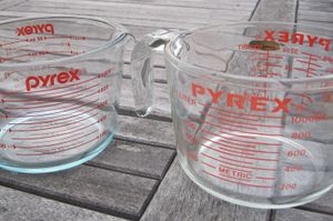 빨간색 텍스트가 있는 두 개의 투명한 계량 저그. 오른쪽 저그는 왼쪽 저그보다 더 넓다.