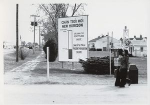 Two women walk past a large sign in Vietnamese and English at an army base