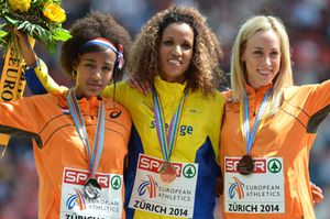 Three women are standing in the podium embracing each other in victory. Hassan in the left with a silver medal.