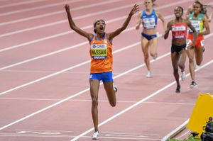 Hassan celebrates crossing the finish line, holding her arms up in front of three other women reaching her.