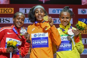 Three woman are on the podium holding their medals. Hassan is in the middle holding a gold medal.