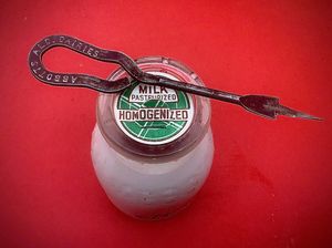 재사용 가능한 반 파인트 유리 우유병은 뾰족한 개봉 도구로 들어 올려진 플랩을 당겨서 열 수 있는 일회용 판지 캡으로 밀봉됨