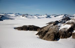 주노, 알래스카 근처 원경. 주변은 산봉우리가 보이는 깨끗한 흰 눈으로 덮여 있다. 이미지 오른쪽, 사진가에 더 가까이, 노출된 암석 노두가 있다.
