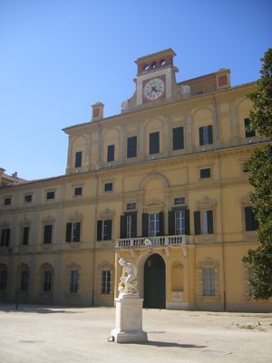 파란 하늘 아래 노란색 르네상스 궁전의 정면, 그 앞에 흰색 대리석 조각상이 있다.