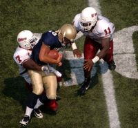 대학 미식축구 경기에서의 태클. 해군의 쿼터백 카이포노아 카헤아쿠엔하다가 매사추세츠의 디펜시브 백 제임스 이헤디그보(7번)와 라인배커 찰스 워커(11번)에게 태클을 당하고 있다.