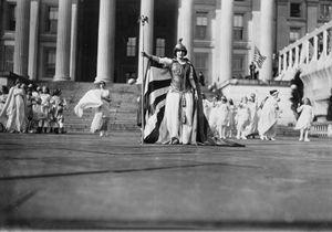  컬럼비아 복장을 한 독일 배우 헤드비가 라이셔가 재무부 청사 앞에 여성 참정권 퍼레이드 참가자들과 함께 서 있다.