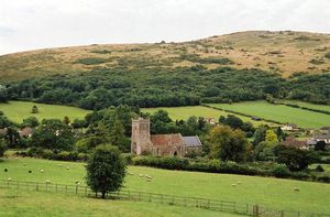 언덕 뒤, 나무와 함께 녹색 들판에 보이는 사각 탑이 있는 교회 건물.