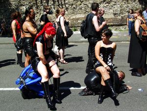 도미나트릭스가 의자처럼 사용하여 복종적인 남성 위에 앉아 있는 모습, 쾰른 프라이드, 2006년.