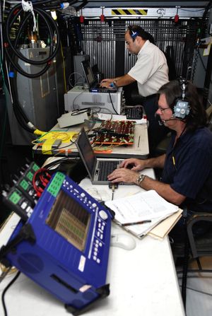 엔진 기술자 피터 존슨과 카를로스 마타 박사가 MLP 내부에서 시간 영역 반사 측정 장비를 작업하고 있다.