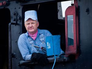 증기 기관차 운전사가 인기 있는 밝은 청색과 흰색 줄무늬 시어서커 작업복과 기관사 모자를 착용하고 있다.