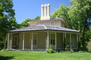 잔디밭과 나무로 둘러싸인 2층짜리 나무 건물, 건물 주변에는 랩어라운드 포치