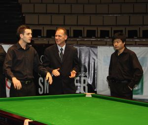 Three men by a snooker table, with Mark Selby on the left and Ding on the right.