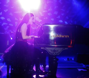 Young woman with long, dark hair singing and playing piano onstage