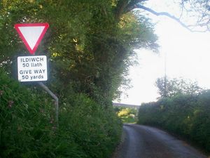 m}}) 앞에 "양보" 교차로가 있음을 알리는 웨일스어와 영어 이중 언어 표지판