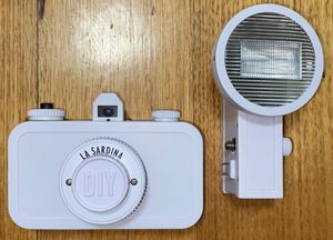 카메라 측면에 나사로 고정되는 호환 가능한 프리츠 더 블리츠 플래시가 있는 흰색 라 사르디나 카메라