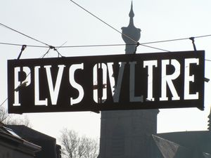 시의 표어 "플러스 울트라". 카니발에서는 틀에 짜인 불꽃놀이가 된다. 뒤쪽은 성 유르스메르 교회