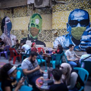 사람들이 2020년 8월 카이로의 한 카페에서 마스크를 쓴 사람들을 묘사한 벽화 앞에서 식사하고 있다