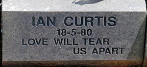 굵은 글씨체로 "이안 커티스, 18-5-80, Love Will Tear Us Apart"라고 새겨진 회색 돌