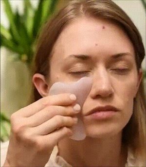 얼굴에 괄사 도구를 사용하는 사람