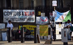 백신 반대 시위자들이 "코로나19 사망자의 60%가 백신 접종자"라고 적힌 노란색 포스터를 들고 시위하고 있다 (음모론 관련 언급 포함)