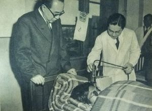 의학 전문가들이 전신 계측 시대 이전, 1954년 3월 31일, 먼지 같은 방사성 낙진을 모았을 머리카락에 가이거 계수기를 사용하여 침대에 누워있는 선원의 방사능을 평가하고 있다.