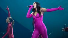 Dua Lipa performing in a pink catsuit surrounded by dancers in red outfits