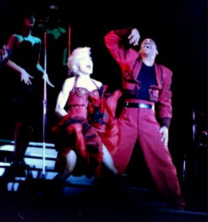 마젠타 재킷과 검은 바지를 입고 오른손에 들고 있는 마이크에 노래하는 마돈나