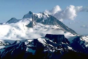 전경의 바위 능선 위로 솟아 있는, 아래쪽 경사면이 심하게 빙하로 덮인 바위 산.