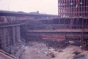 1969년, 북서쪽에서 바라본 초기 세계 무역 센터 배스터브 공사 현장. 앞쪽에는 임시 가교 위에 지지된 PATH 동쪽 터널 F가 보인다. 왼쪽에는 타이백이 있는 슬러리 벽이 보이며, 배경에는 북쪽 타워의 골조가 보인다. 현재의 웨스트 스트리트 위에 있던 철거된 서쪽 고가도로도 확인할 수 있다.