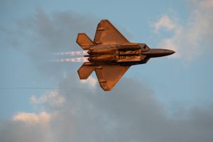 USAF F-22 랩터가 애프터버너를 완전히 켠 상태로 에어벤처 상공에서 고속 저고도 비행을 하며 충격 다이아몬드가 저녁 노을에 비치는 모습