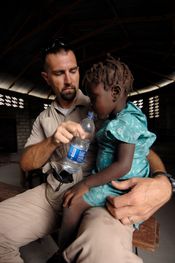 NCIS 특별 수사관이 2008년 아이티에서 허리케인 구호 작전 중 현지 마을의 의료 평가를 하는 동안 USS 키어사지에 배속되어 한 소녀에게 물을 주고 있다.