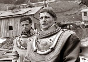 헬멧 연결을 위한 중단된 나사산과 슈트에 고정하는 브레이스 링을 보여주는 코르셋. 배경에 12볼트, 전경에 6볼트.