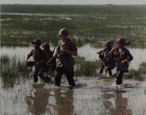 1964년 8월 27일, 제1대대 52연대 소속 기관총 분대와 미군 고문이 논밭을 건너고 있다.