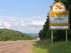 4차선 고속도로 옆 표지판에 "메릴랜드에 오신 것을 환영합니다. 저희는 사업을 시작했습니다. 래리 호건 주지사"라고 적혀 있습니다.