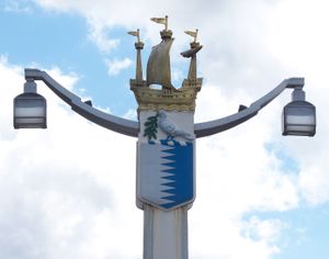 두 개의 팔 끝에 두 개의 램프를 들고 있는 기둥. 기둥 상단은 갤리온으로 장식되어 있으며, 배 아래에는 꺾은 선으로 분리된 흰색 왼쪽과 파란색 오른쪽이 포함된 방패가 있고, 그 위에 올리브 가지를 들고 있는 흰색 새가 놓여 있다.