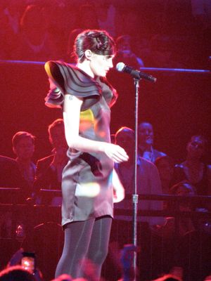 33세의 블라스코는 3/4 샷과 오른쪽 프로필로 묘사되어 있다. 그녀는 마이크 스탠드 위로 내려다보고 있다. 그녀의 드레스는 어두운 배경에 색색의 부분이 섞여 있다. 그녀의 오른팔은 팔꿈치에서 구부러져 있다. 작은 문신이 그녀의 오른쪽 팔 위쪽에 부분적으로 보인다.