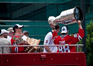 패트릭 케인이 스탠리 컵을 들어올리고 조나단 투스가 콘 스마이스 트로피를 들고 있는 블랙호크스 우승 퍼레이드 모습.
