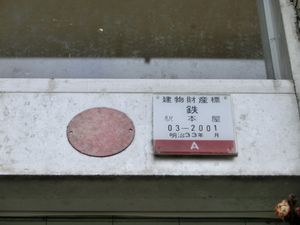 쇼와 시대에 지어진 건물의 정면 입구에 있는 금속제 도어 프레임에 붙어 있는 메이지 33년의 건물 재산표