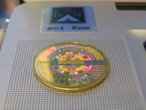 변조 방지 보안 홀로그램 아래에 개인 키가 숨겨진 황동 토큰. 홀로그램의 투명한 부분을 통해 주소의 일부가 보입니다.